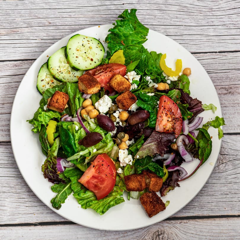 A vibrant Mediterranean salad with lettuce, cucumbers, tomatoes, chickpeas, olives, feta, and croutons.
