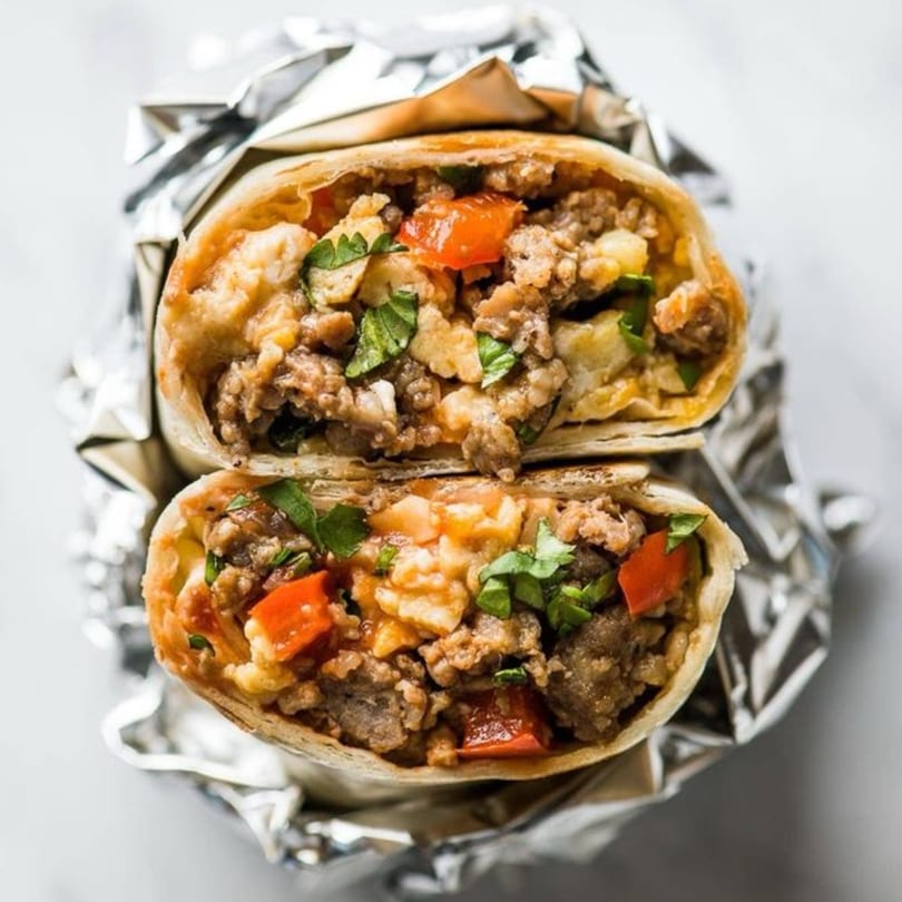 A Mediterranean burrito, cut in half, revealing seasoned meat, red peppers, and herbs wrapped in foil.