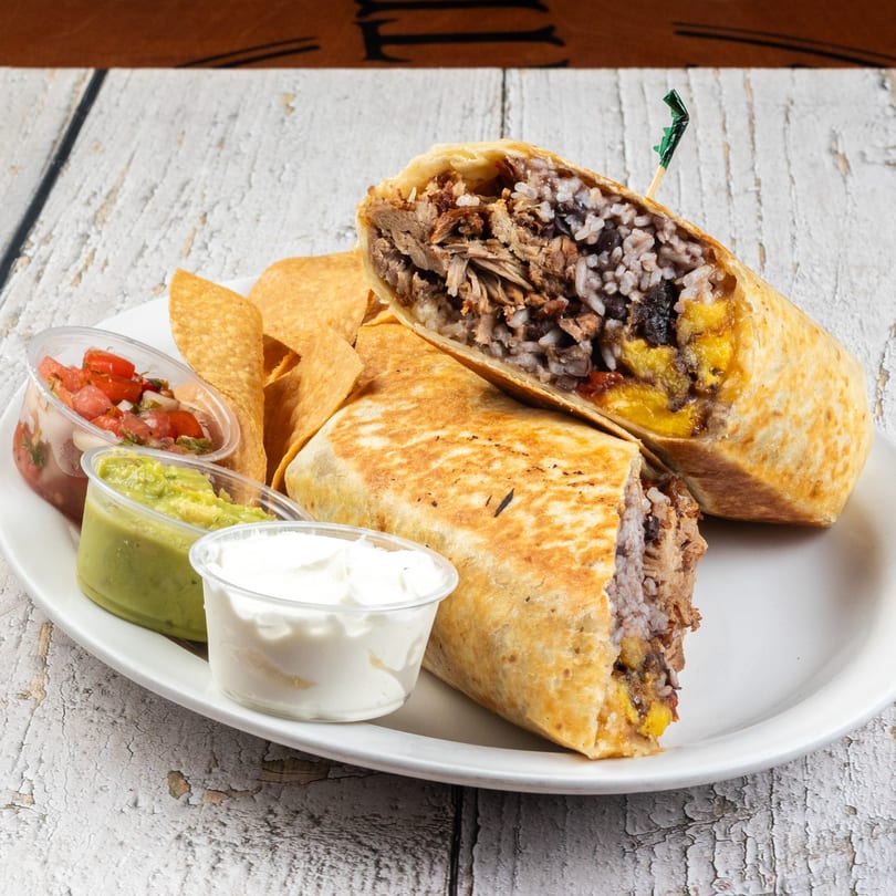 Two burritos, one cut open, with tortilla chips, salsa, guacamole, and sour cream on a white plate.